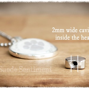 May include: Silver heart-shaped pendant necklace with a paw print design. The pendant has a 2mm wide cavity inside the heart.