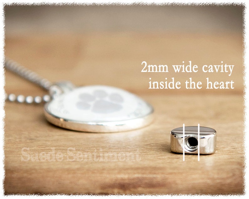 May include: Silver heart-shaped pendant necklace with a paw print design. The pendant has a 2mm wide cavity inside the heart.