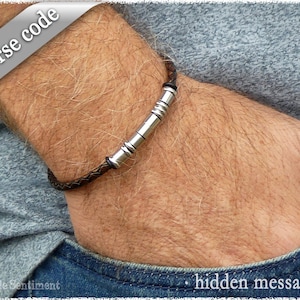 May include: A brown leather bracelet with a silver metal bar that has a hidden message in Morse code.