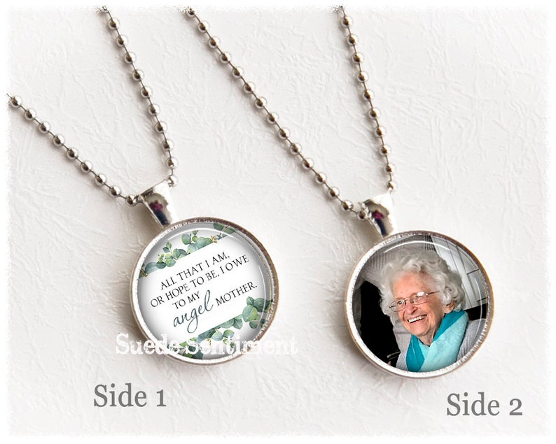 May include: A silver chain necklace with two round pendants. One pendant features a photo of an older woman smiling. The other pendant has a white background with green foliage and the text "ALL THAT I AM, OR HOPE TO BE, I OWE TO MY angel MOTHER."