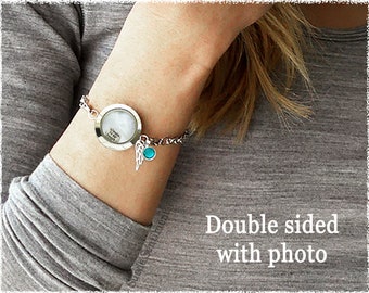 May include: Silver charm bracelet with a round locket that can hold a photo. The locket has a small angel wing charm and a turquoise blue bead.