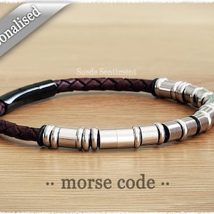 Peut inclure: Un bracelet en cuir marron avec des perles en métal argenté. Le bracelet a un fermoir noir et le texte "... morse code ..." est imprimé sous le bracelet.