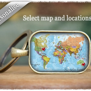 Peut inclure: Un porte-clés avec une carte du monde et deux cœurs rouges marquant des emplacements. Le porte-clés est en métal et a une finition bronze. Le texte "Select map and locations" est visible en haut de l'image.