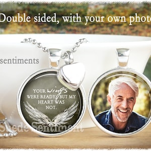 May include: A silver necklace with a round pendant featuring a photo on one side and a sentiment on the other. The sentiment reads "Your wings were ready but my heart was not." The pendant is attached to a silver chain with a heart-shaped charm.