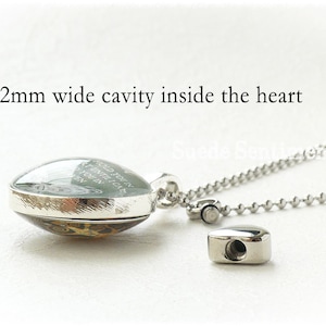 May include: A silver heart-shaped locket with a glass front and a silver chain. The locket has a 2 mm wide cavity inside and the glass front has an inscription that reads "Hold you in my heart until I can hold you in my arms again".