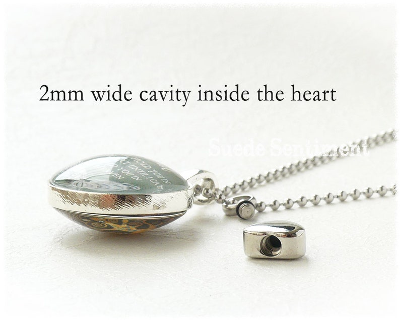 May include: A silver heart-shaped locket with a glass front and a silver chain. The locket has a 2 mm wide cavity inside and the glass front has an inscription that reads "Hold you in my heart until I can hold you in my arms again".
