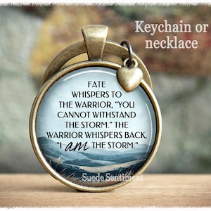 May include: A bronze-toned keychain or necklace with a glass charm featuring a quote about facing challenges. The quote reads: "Fate whispers to the warrior, 'You cannot withstand the storm.' The warrior whispers back, 'I am the storm.'"