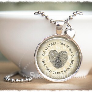 May include: Silver necklace with a round pendant featuring a fingerprint heart design and the text "Always be close at heart - side by side or miles apart".