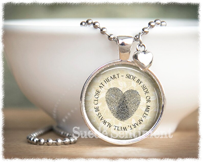 May include: Silver necklace with a round pendant featuring a fingerprint heart design and the text "Always be close at heart - side by side or miles apart".