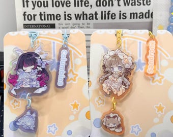 May include: Two acrylic charms featuring anime-style characters on display cards. The left charm depicts a character with dark hair and purple accents labeled Columbina. The right charm shows a character with light hair labeled Sandrone.