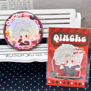 以下が含まれることがあります： 白い髪のキャラクターのホログラフィックイラストと「QinChe」の文字が描かれた円形のピンバッジと、同じキャラクターがグラスを持ち「QinChe」「I have got you」と書かれた長方形のカード。