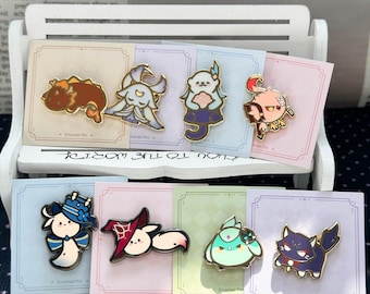 May include: A collection of eight colorful enamel pins featuring various stylized cartoon characters, each mounted on an individual square backing card with a thin border, displayed on a small white decorative bench.