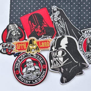 Puede incluir: Una colección de parches de tela bordados con personajes y símbolos de Star Wars, incluyendo a Darth Vader, un Stormtrooper y el texto Sith Lord, 501st Legion y Death Star, en colores de hilo negro, blanco, rojo y dorado.