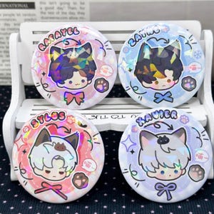 以下が含まれることがあります： 猫耳をつけたアニメ風キャラクターのホログラムイラストが描かれた4つの円形缶バッジ。各バッジにはRafayel、Zayne、Sylus、Xavierの名前が記されており、肉球、リボン、小さな日本語の文字記号が添えられています。
