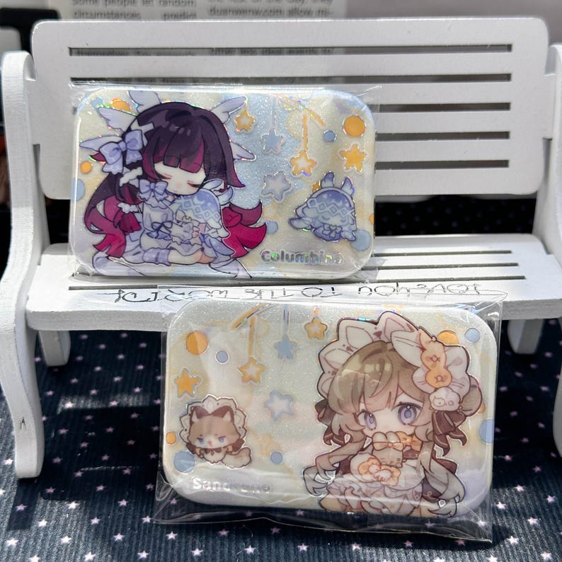 May include: Two rectangular pins featuring anime-style illustrations. The top pin shows a character with dark hair and purple accents labeled Columbina. The bottom pin shows a character with light brown hair labeled Sandrone, both with stars.