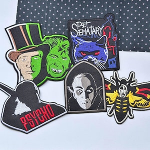 May include: Five embroidered patches featuring horror themes: a split-face character in a top hat, a cat with red eyes labeled Pet Sematary, a silhouette with red Psycho text, a vampire portrait, and a yellow and black moth with a skull pattern.
