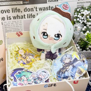 Può includere: Una scatola regalo contenente un peluche con cappuccio a forma di cono gelato verde menta, un espositore in acrilico dorato, una spilla circolare con un personaggio anime e vari piccoli adesivi su paglia di carta.
