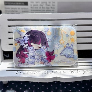 May include: A rectangular pin featuring a glittery finish and an anime-style illustration of a character with dark purple hair and pink highlights, wearing a white outfit with bows. The text Columbina is printed in blue near a small creature.
