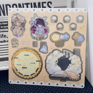 May include: A square sticker sheet with a light peach background featuring various die-cut designs including two anime-style characters, a large round pie, a cloud-shaped frame with a book, small flowers, and stars with holographic accents.