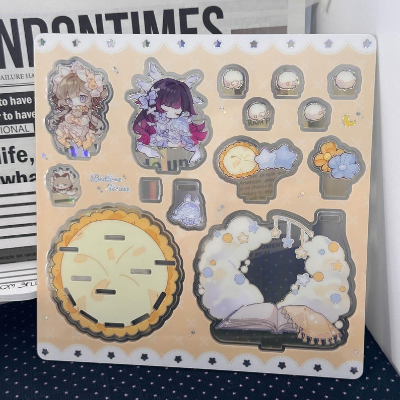 May include: A square sticker sheet with a light peach background featuring various die-cut designs including two anime-style characters, a large round pie, a cloud-shaped frame with a book, small flowers, and stars with holographic accents.