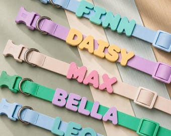 May include: Five pet collars in light blue, lavender, beige, green, and light blue, each featuring a plastic buckle, a metal D-ring, and a sliding adjuster. The collars are personalized with raised, block-letter names: FINN, DAISY, MAX, BELLA, and LEO.