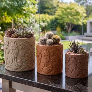 Może przedstawiać: Trzy cylindryczne ceramiczne doniczki w odcieniach beżu, terakoty i brązu, każda z wytłoczonymi motywami lisów i jesiennych liści. Doniczki zawierają różne sukulenty i kaktusy, w tym pasiastą haworthię oraz okrągłe kaktusy.
