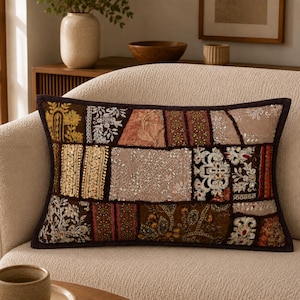 May include: A rectangular throw pillow featuring a patchwork design of various fabric panels in shades of brown, gold, beige, and cream. The surface is decorated with intricate embroidery, metallic thread work, sequins, and floral patterns.