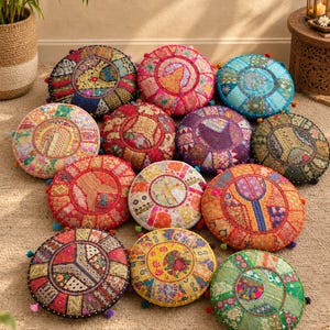 May include: A collection of twelve round floor cushions featuring intricate patchwork designs with vibrant embroidery, metallic thread accents, and small colorful tassels along the edges. Each cushion displays a unique combination of geometric patterns and floral motifs in various colors including red, blue, yellow, green, and purple.