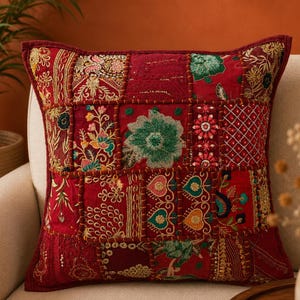 May include: A square throw pillow featuring a patchwork design of deep red fabric panels. Each panel is decorated with intricate embroidery in gold, green, and pink thread, showcasing floral motifs, geometric patterns, and heart-shaped details.