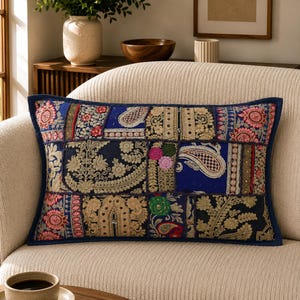 Könnte beinhalten: Ein rechteckiges Zierkissen mit einem Patchwork-Design aus verschiedenen Stoffbahnen. Das Textil zeigt aufwendige Goldstickereien, Paisleymuster und florale Motive in den Farben Dunkelblau, Schwarz, Rot und Grün, eingefasst von einer dunkelblauen Bordüre.