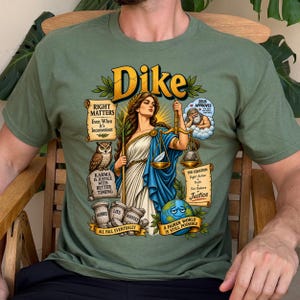 May include: An olive green t-shirt featuring a graphic of the Greek goddess Dike holding scales. The design includes text such as Right Matters, Karma is Justice, and Zeus Approves, alongside illustrations of an owl, a globe, and stone pillars.