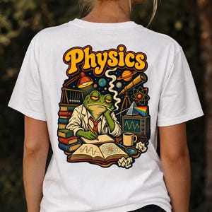 Op de afbeelding: Een wit t-shirt met een kleurrijke afbeelding op de achterkant. Het ontwerp toont een groene kikker in een laboratoriumjas die in een notitieboek schrijft, omringd door natuurkundige voorwerpen zoals boeken, een telescoop, een prisma, een monitor en het woord Physics.