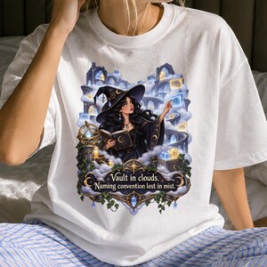 Puede incluir: Una camiseta blanca con el gráfico de una bruja con sombrero negro sosteniendo un libro entre nubes y arcos de piedra. El diseño incluye el texto Vault in clouds. Naming convention lost in mist, enmarcado por detalles ornamentados en dorado y azul.