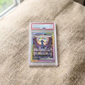 Puede incluir: Una carta coleccionable Pokemon Pre En Umbreon ex Special Illustration Rare de 2025, graduada y sellada en una funda de plástico transparente. La carta muestra un personaje Umbreon oscuro con un aura circular colorida y el texto Moon Mirage y Onyx.