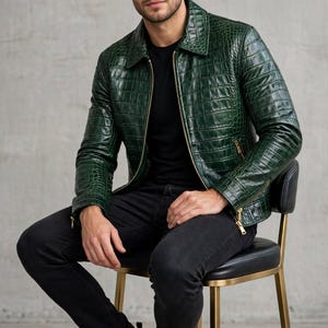 May include: A dark green jacket with a textured crocodile skin pattern, featuring a classic collar, long sleeves, and a gold-toned front zip closure. The jacket includes zipped side pockets and zipped cuffs, worn with a black shirt and trousers.