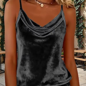 Könnte beinhalten: Ein dunkelgraues Samt-Camisole mit Wasserfall-Ausschnitt und dünnen Spaghettiträgern. Das Oberteil hat eine weiche, strukturierte Oberfläche und wird mit einer hellblauen Jeans kombiniert. Das Kleidungsstück ist ärmellos.