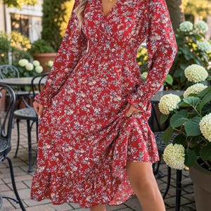 Può includere: Un abito midi a maniche lunghe in tessuto rosso vivace con un motivo floreale su piccola scala nei toni del bianco, blu e giallo. L'abito presenta uno scollo a V, una vita elasticizzata arricciata e un orlo a balze che aggiunge volume.