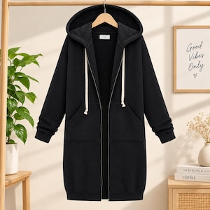 May include: A long-length black zip-up hoodie featuring a hood with thick white drawstrings, long sleeves with ribbed cuffs, and two front patch pockets. The garment is constructed with a full-length front zipper and a straight hemline.
