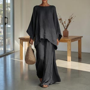 Peut inclure: Un ensemble deux pièces gris anthracite composé d'un haut ample à manches longues avec une encolure large et d'un pantalon assorti à jambes larges doté de fentes latérales. La tenue est accompagnée d'un sac à main tissé marron clair.