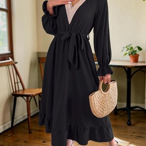 Può includere: Un abito midi nero con maniche lunghe e polsini arricciati, scollo a V rifinito con pizzo all'uncinetto beige e una cintura in tessuto abbinata in vita. La gonna presenta un orlo arricciato ed è abbinato a una borsa in paglia intrecciata.