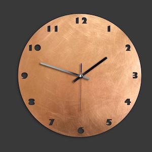 May include: A round wall clock with a copper-coloured face, black hour and minute hands and black numbers. The clock face has a brushed metal finish.