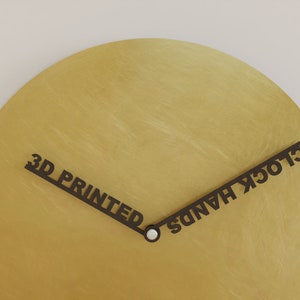 May include: A gold-coloured clock face with black 3D printed hands that read "3D PRINTED" and "CLOCK HANDS".