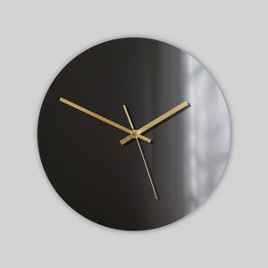 Puede incluir: Un reloj redondo negro con agujas doradas. La esfera del reloj es lisa y no tiene números.