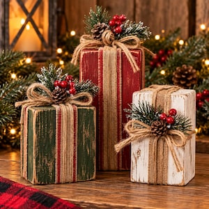 May include: Three rectangular wooden blocks painted in red, green, and white with a distressed finish. Each block is wrapped with a burlap ribbon and topped with a decorative cluster of artificial pine needles, small pinecones, and red berries.