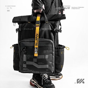 May include: A black roll-top backpack featuring a prominent yellow vertical strap with Japanese text, side pockets with yellow drawstrings, and a front compartment printed with the text KREMLIN GENESIS LAB and ARTIFICIAL INTELLIGENCE in white.