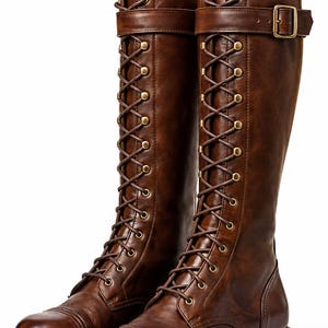 Könnte beinhalten: Ein Paar kniehohe braune Stiefel mit Schnürung vorne, messingfarbenen Ösen und passenden braunen Schnürsenkeln. Die Stiefel verfügen über einen Zierriemen mit messingfarbener Schnalle am Schaft, eine abgerundete Zehenkappe und eine dicke Profilsohle.