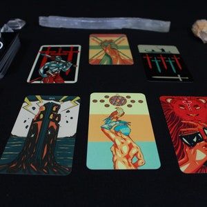 May include: Tarot card spread with ten cards laid out on a black surface. The cards feature colorful illustrations of various figures and symbols, including a tower, a lion, and a hand holding a sword.