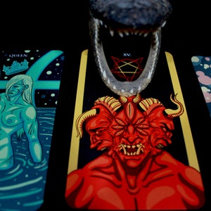 May include: Three tarot cards with colorful illustrations. The card on the left shows a woman with a crown, the middle card shows a red demon with multiple eyes and horns, and the card on the right shows a man with a blue background.
