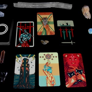 May include: Tarot card spread with ten cards laid out on a black surface. The cards are from a deck with colorful illustrations and include the Tower, the Devil, the Three of Swords, the Two of Swords, the Five of Swords, the King of Swords, the World, and the Strength card. There are also several crystals and a long, white, rectangular object on the surface.