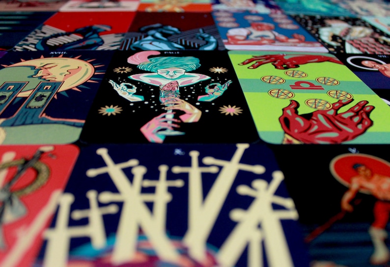 May include: A close-up of a tarot card deck with various cards spread out. The cards feature colorful illustrations and intricate designs. The cards are arranged in a grid pattern, with the top row showing the cards "VIII", "PAGE", "LIBRA", and "THE WORLD".